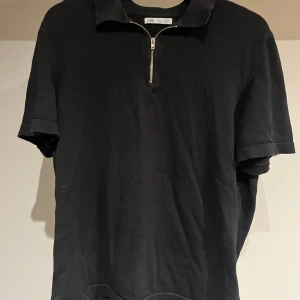 Svart pikétröja med dragkedja från Zara - Svart pikétröja från Zara i bomull med klassisk krage och snygg half zip-dragkedja framtill. Tröjan har korta ärmar och en clean look som passar perfekt till jeans eller shorts. Enkel och stilren design för en chill vibe. Bra skick! Bara att höra av sig vid eventuella frågor!😉