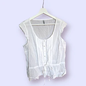 Blus i storlek L, vintage - Vit ärmlös blus med broderade detaljer och knäppning samt snörning framtill.