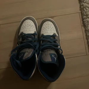 Nike Air Jordan 1 Mid blå/vit/grå Nypris 2000 Ca! - Nike Air Jordan 1 Mid i en clean färgkombo av blått, vitt och grått. Klassisk siluett med blå swoosh, snörning och perforerad tåbox. Skorna har en platt sula och är tillverkade i skinn och syntet. Perfekta för dig som vill sticka ut med en ikonisk sneaker.