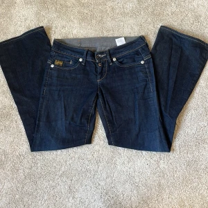 Mörkblå bootcut jeans från G-Star - Snygga mörkblå jeans från G-Star. De är boot cut och väldigt lågmidjade, de sitter även väldigt snyggt på. Säljer pga att de är lite för korta för mig. De är stl 27/32 och jag är ca 165. Pris kan diskuteras och de är bara att höra av sig om ni vill ha fler bilder exempel på eller andra vinklar osv. 