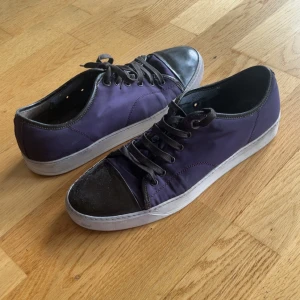 Lila sneakers från Lanvin med svart tå - Snygga sneakers från Lanvin i lila textil med svarta skinn-detaljer på tån och svarta snören. Klassisk låg modell med vit sula och rund tå. Perfekta för dig som gillar stilrena men unika sneakers med lyxig känsla.