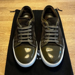 Lanvin sneakers  - Snygga sneakers från Lanvin i mörkgrön mocka med glansig lackad tå och vita sulor. Skorna har grå snörning och en klassisk låg profil. Perfekta för dig som gillar exklusiva detaljer och stilren design.
