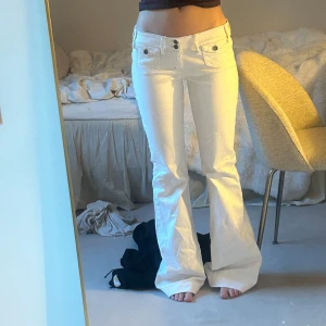 Vita lågmidjade bootcut jeans  - Säljer ett par vita jeans med låg midja och bootcut-ben. Byxorna har dubbla knappar framtill, fickor med lock och snygga sömdetaljer. Midjemått-37 cm Innerbenslängd-80 cm. 