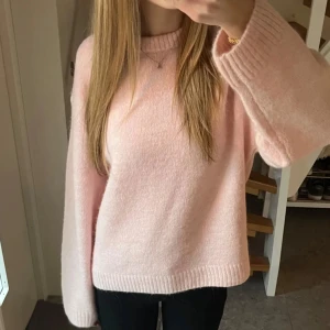 Ljusrosa stickad tröja - Supermysig ljusrosa stickad tröja med rund hals och långa ärmar. Tröjan har en relaxed passform och ribbade muddar vid ärmslut och nederkant. Perfekt för att hålla sig varm och snygg under kyliga dagar.