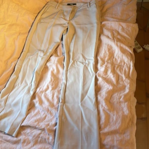 Beigea kostymbyxor från Bikbok  - Snygga ljusbeige kostymbyxor med klassiska pressveck och hällor för bälte. Byxorna har raka ben och diskreta bakfickor. Perfekta för en clean och stilren look. Lite nopprig kring knävecken men inget man ser och kan säkert noppra bort! Används en gång. 