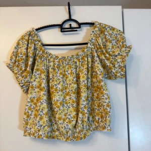 Offshoulder blus  - Supersöt blommig blus från Gina Tricot med gula och grå blommor på vit botten. Modellen är offshoulder med korta puffärmar och resår i både halsringning och nederkant. Perfekt för sommarens alla häng och picknickar! Finns inga defekter. Pris kan diskuteras.