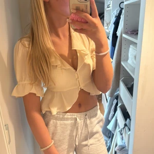 Ljusgul croppad blus med volang - Superfin ljusgul blus med korta volangärmar och v-ringning. Croppad modell med knappar framtill och volangdetaljer längs krage och ärmslut. Perfekt för dig som gillar en söt och trendig look.