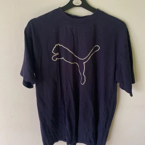 Mörkblå Puma t-shirt med logga - Snygg mörkblå t-shirt från Puma med stor vit konturerad logga på bröstet. Klassisk passform och rund halsringning, perfekt för en sportig och avslappnad stil. Tillverkad i mjuk bomull för skön känsla hela dagen.