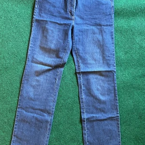 Blå jeansbyxor från Time, stl 44L - Säljer ett par blå jeansbyxor från Time i storlek 44L. Byxorna har raka ben och snygga broderade detaljer i rött och gult på bakfickorna. Klassisk femficksmodell med kontrastsömmar och normal passform. Perfekta för dig som gillar stilrena jeans med en twist.