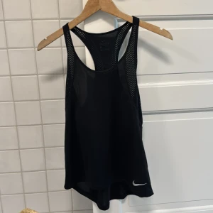 Svart Nike Dri-FIT linnetopp S - Svart sportigt linne från Nike med Dri-FIT-teknologi. Sval mesh på sidorna och racerback-rygg för extra ventilation. Liten vit Nike-logga framtill. Perfekt för dig som vill ha en lätt och luftig topp till träningen.