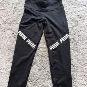 Svarta leggings från Puma med logga - Svarta leggings från Puma med bred midja och vit PUMA-logga på båda benen. Köpta från stadium använd ngt par gånger☺️