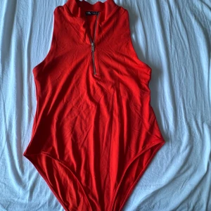 Röd ärmlös bodysuit från Zara - Snygg röd bodysuit från Zara med hög krage och dragkedja framtill. Modellen är ärmlös och sitter tight inte använd så mycket