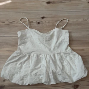 Vit linnetopp från H&M Divided - Supersöt vit linnetopp från H&M Divided med tunna, justerbara axelband och volangliknande nederdel. Toppen är i flowy passform som är perfekt för varma dagar. Enkel och stilren design som är lätt att matcha.