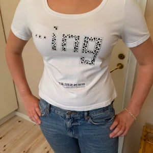 Vit croppad topp från ADA Fashion - Säljer en vit croppad topp från ADA Fashion med kort ärm och rund halsringning. Framsidan har ett coolt tryck. Perfekt till jeans för en avslappnad och trendig look.