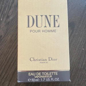 Dune Pour Homme Eau de Toilette 50ml - Dune Pour Homme från Christian Dior är en klassisk herrparfym i en stilren, transparent glasflaska med svart rund kork. Doften är fräsch och maskulin, perfekt för dig som gillar eleganta och tidlösa parfymer. Flaskan rymmer 50 ml Eau de Toilette.