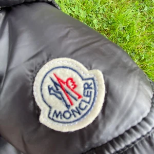 Svart Moncler dunjacka, storlek S - Säljer en svart dunjacka från Moncler i storlek S. Jackan har klassisk Moncler-logga på ärmen och coolt serietidningsfoder på insidan. Perfekt för dig som vill ha en stilren och varm jacka med exklusiv känsla. Materialet är glansigt och jackan har en modern look.