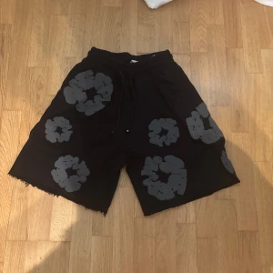 Denim tears shorts - Coola svarta shorts med unikt grått blommönster över hela tyget. Modellen är loose fit med råa kanter nertill och elastisk midja med snörning. Perfekta för en avslappnad och trendig stil under sommaren. ⚠️1:1⚠️