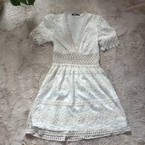 Vit spetsklänning från Gina Tricot - Superfin vit kortklänning från Gina Tricot med v-ringning, spetsdetaljer och markerad midja. Klänningen har korta ärmar med vacker spetskant och broderade detaljer över hela plagget. Den har lite smink fläckar i halsen, men inget man tänker på när den är på. Andvänts två gånger 