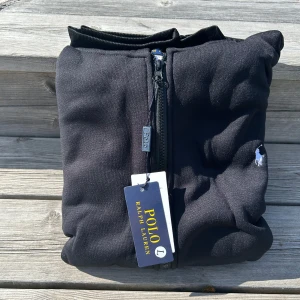 Svart hoodiejacka från Polo Ralph Lauren - Svart hoodiejacka med Polo Ralph Lauren märke med dragkedja, huva med snörning och broderad logga på bröstet. Perfekt för en stilren look. (Vet ej om den äkta)