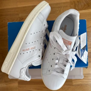 Adidas Stan Smith vita sneakers, oanvända  - Vita Adidas Stan Smith med tryck i kopparmetallic. Köpta för några år sen men oanvända (för små) med lappar kvar. Köpta för 1350 kr så passa på 🔥öppen för prisförslag. Klassisk clean sko, passar till allt. Det går att se lite på skinnet att de är provade om man tittar noga, se bilder. Hör av dig vid frågor 💕