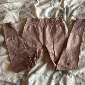 Rosa seamless leggings från lager - Säljer ett par seamless leggings från lager i en snygg ljusrosa nyans. De har hög midja, ribbade detaljer och är tillverkade i ett stretchigt syntetmaterial som sitter tight och bekvämt. Perfekta för träning eller chill dagar. Har ett litet håll nere vid small benen! Storlek 134/140