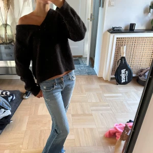 Svart offshoulder stickad tröja - Mysig svart stickad tröja med offshoulder-design och lång ärm. Tröjan är croppad och har en loose passform, perfekt för dig som gillar en avslappnad men ändå trendig look. Passar grymt till jeans eller kjol.