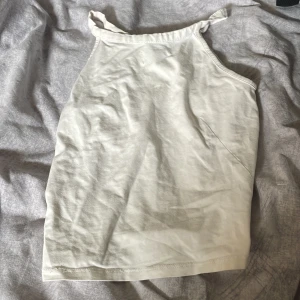 Vit ärmlös linnetopp - En stilren vit linnetopp med smala axelband och knyt på axlarna. Toppen har rak passform och är tillverkad i mjuk bomull, perfekt för varma dagar. Enkel och clean look som passar till jeans eller kjol.