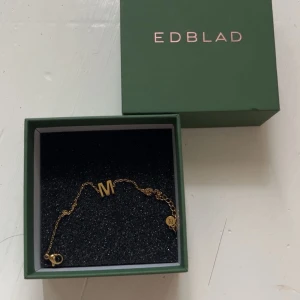 Guldarmband med M från Edblad - Snyggt armband i guld från Edblad med ett M som detalj. Tunt kedjearmband med justerbar längd och liten rund Edblad-tag vid låset. 