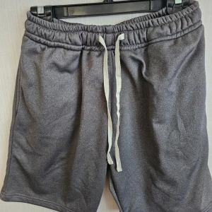 Grå shorts från Project XY, XL - Mysiga grå shorts från Project XY i storlek XL. De har elastisk midja med vit snörning, sidofickor och en bakficka. Perfekta för chill dagar eller träning, tillverkade i mjukt material som känns skönt mot huden.