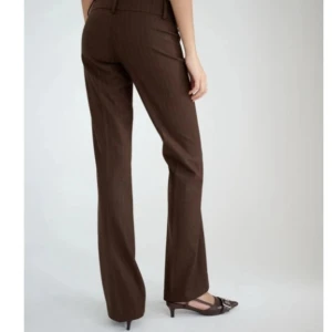 Bruna kostymbyxor med raka ben - Snygga bruna kostymbyxor med klassisk rak passform och pressveck. Byxorna har hällor för bälte och diskreta fickor bak. Perfekta för en clean och stilren look. Helt oanvända och slutsålda på hemsidan!