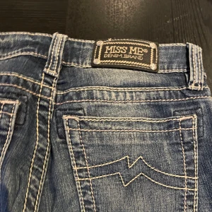 Miss Me skinny jeans blå, stl 26 - Snygga skinny jeans från Miss Me i klassisk blå denim med slitningar och kontrastsömmar. Jeansen har låg midja, fem fickor och coola detaljer på bakfickorna. Perfekta för dig som gillar en smal passform och vill sticka ut lite extra.