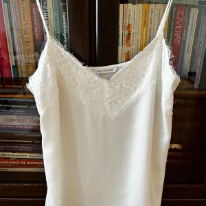 Vit spetslinnetopp från KappAhl - Supersöt vit linnetopp från KappAhl med tunna axelband och v-ringning dekorerad med romantisk spets. Perfekt för lager på lager eller till jeans. Lätt och luftig känsla, passar till många stilar.