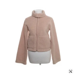 Beige teddyjacka med dragkedja - Mysig beige teddyjacka med hög krage och hel dragkedja framtill. Jackan har två stora fickor och är tillverkad i fluffigt teddy-material som ger en chill och trendig look. Perfekt för lager-på-lager och passar till allt från jeans till mjukisbyxor.