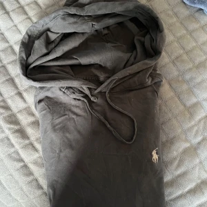Svart hoodie från Ralph Lauren - Säljer en svart hoodie från Ralph Lauren med klassisk huva och dragsko. Tröjan har långa ärmar och den ikoniska broderade loggan på bröstet. Tillverkad i mjuk bomull, perfekt för chill dagar eller när du vill ha en clean look.