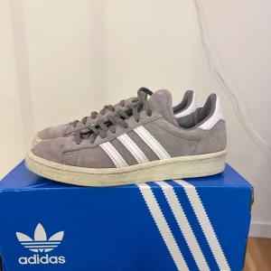 Grå adidas sneakers mocka - Snygga adidas sneakers i grå mocka med klassiska vita ränder och vit häl. Skorna har rund tå, platt sula och grå snörning. . Kommer med kartong