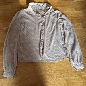 Beige blus med struktur från NA-KD - Säljer en ljusbeige blus från NA-KD i storlek 36. Skjortan har diskret strukturmönster, klassisk krage och knäppning framtill. Långa ärmar med manschett och knappar. Tunt och luftigt material som känns skönt mot huden.