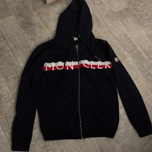 Moncler hoodie med dragkedja - Snygg  hoodie från Moncler i storlek M  ,Tröjan har broderad Moncler-logga på bröstet, går att pruta ner vid snabb affär. Aldrig använd då den är för stor för mig