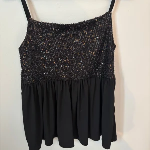 Svart paljettlinne från Gina Tricot - Supersnygg svart linne från Gina Tricot med glittriga paljetter upptill och volang nertill. Den är i storlek 158/164 och är i väldigt bra skick.💓