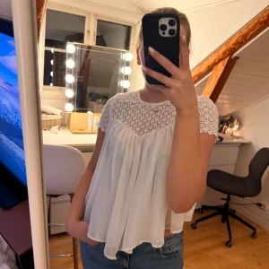 Vit spetsblus från Zara Trafaluc XS - Superfin vit blus från Zara Trafaluc i storlek XS. Toppen har korta ärmar, spets upptill med blommigt mönster och en flowy, luftig nederdel i tunt tyg. Perfekt för dig som gillar romantisk och söt stil. Knytning i nacken för extra detalj.