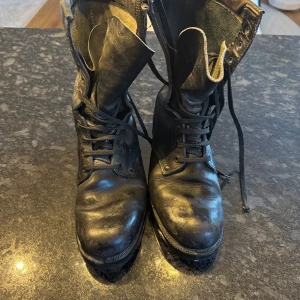 Svarta klassiska militärkängor i äkta skinn - Tunga svarta kängor i äkta skinn med snörning hela vägen upp och robust platt sula. Perfekta för dig som gillar en rå och tidlös look. Hög modell som ger stabilitet och attityd till outfiten. Nypris 450$