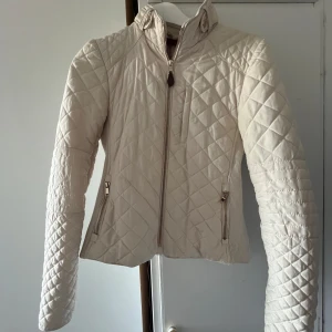 Beige quiltad jacka med dragkedja // Zara // 34/Xs - Nyskick!! Snygg beige quiltad jacka med hög krage och dragkedja framtill. Jackan har långärmade ärmar, två fickor med dragkedja och en extra bröstficka. Den har en figurnära passform och coola detaljer vid kragen. Perfekt för dig som gillar stilren och sportig look. Storlek M men skulle säga mer S 