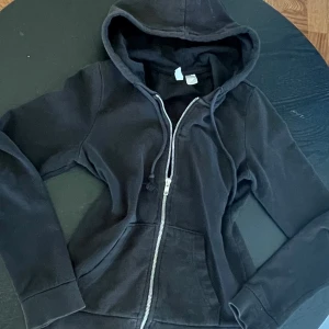 Svart hoodie med dragkedja och huva - Svart hoodie med dragkedja framtill och huva med snörning. Aldrig använd av mig så fint skick, men inte ny. Pris går att diskutera! 💕