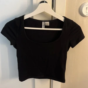Svart croppad topp från H&M Divided - En svart croppad topp från H&M Divided med rundad, djup urringning och korta ärmar. Enkel och stilren design i mjuk bomull, perfekt till jeans eller kjol. Sitter tajt och har en basic vibe som funkar till många olika looks.❤️