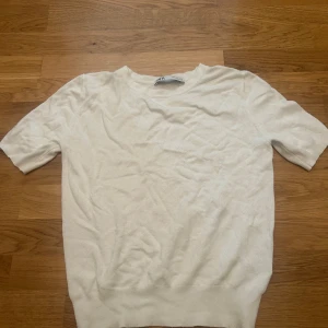 Vit kortärmad tröja från Zara - Enkel och stilren vit tröja från Zara i storlek S. Tröjan har korta ärmar och rund halsringning, perfekt för en clean och fräsch look. Tillverkad i mjukt material som känns skönt mot huden. Passar till många olika outfits.