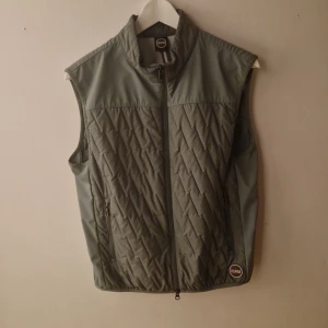 Grå quiltad dunväst från Colmar - Snygg grå dunväst från Colmar med quiltat mönster och dragkedja framtill. Västen har ståkrage, två fickor med dragkedja och Colmar-logga på bröstet. Perfekt lager-på-lager-plagg med sportig vibe och stilren look.