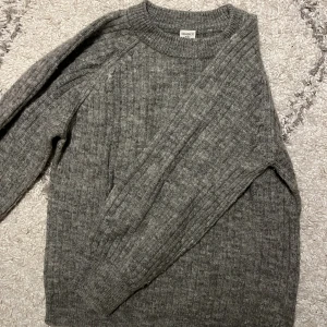 Grå ribbstickad tröja från Lindex - Säljer en grå ribbstickad tröja från Lindex i storlek 128. Tröjan har rund hals och långa ärmar, perfekt för kyliga dagar. Materialet är mjukt och stickat, vilket gör den både bekväm och snygg. Passar dig som gillar enkel och stilren look.