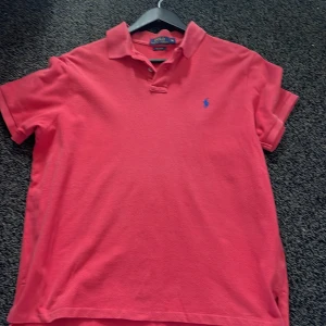 Rosa/röd Polo Ralph Lauren t-shirt XL - Snygg rosa t-shirt från Polo Ralph Lauren i klassisk pikémodell med korta ärmar och krage. Broderad blå logga på bröstet och custom fit-passform. Perfekt för dig som gillar stilren och sportig vibe. Storlek xl men passar mer L därför är priset nersänkt!👍🏻