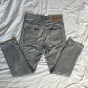 Grå loose fit jeans Jack & Jones - Snygga grå jeans från Jack & Jones i modellen Loose Chris. De har loose fit, raka ben och klassisk femficksdesign. Jeansen är tillverkade i bomull och har en cool, ljusgrå tvätt som passar till allt. Perfekta för dig som gillar avslappnad look. Jeansen har några små skador längst ner på benet. Kolla 5:te bilen. Annars bra skick