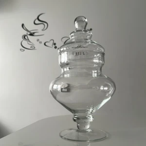 Klar glasburk med lock - Stilren och dekorativ glasburk i transparent glas med rundad form och fot. Perfekt som inredningsdetalj eller för att förvara småsaker. Burken har ett matchande lock med knopp upptill för enkel öppning.