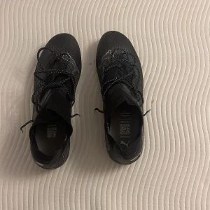 Svarta fotbollsskor från Puma - Säljer ett par svarta fotbollsskor från Puma med coola vita detaljer och snörning. Skorna har stickad ovandel och mönstrad sula med dobbar för grymt grepp på planen. Perfekta för dig som vill ha stilrena och funktionella skor till matchen. Köpte för 2000 